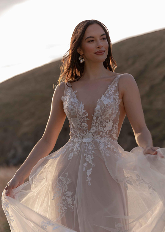 Frech lässt das Model ihr Brautkleid im Wind wehen, während im Hintergrund der Strand zu erkennen ist, an dem es steht.